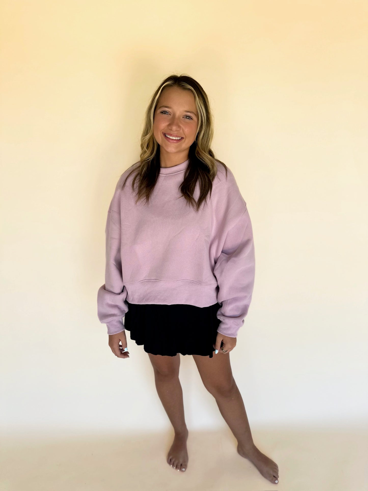 Person wearing a light purple sweatshirt and black shorts against a plain background