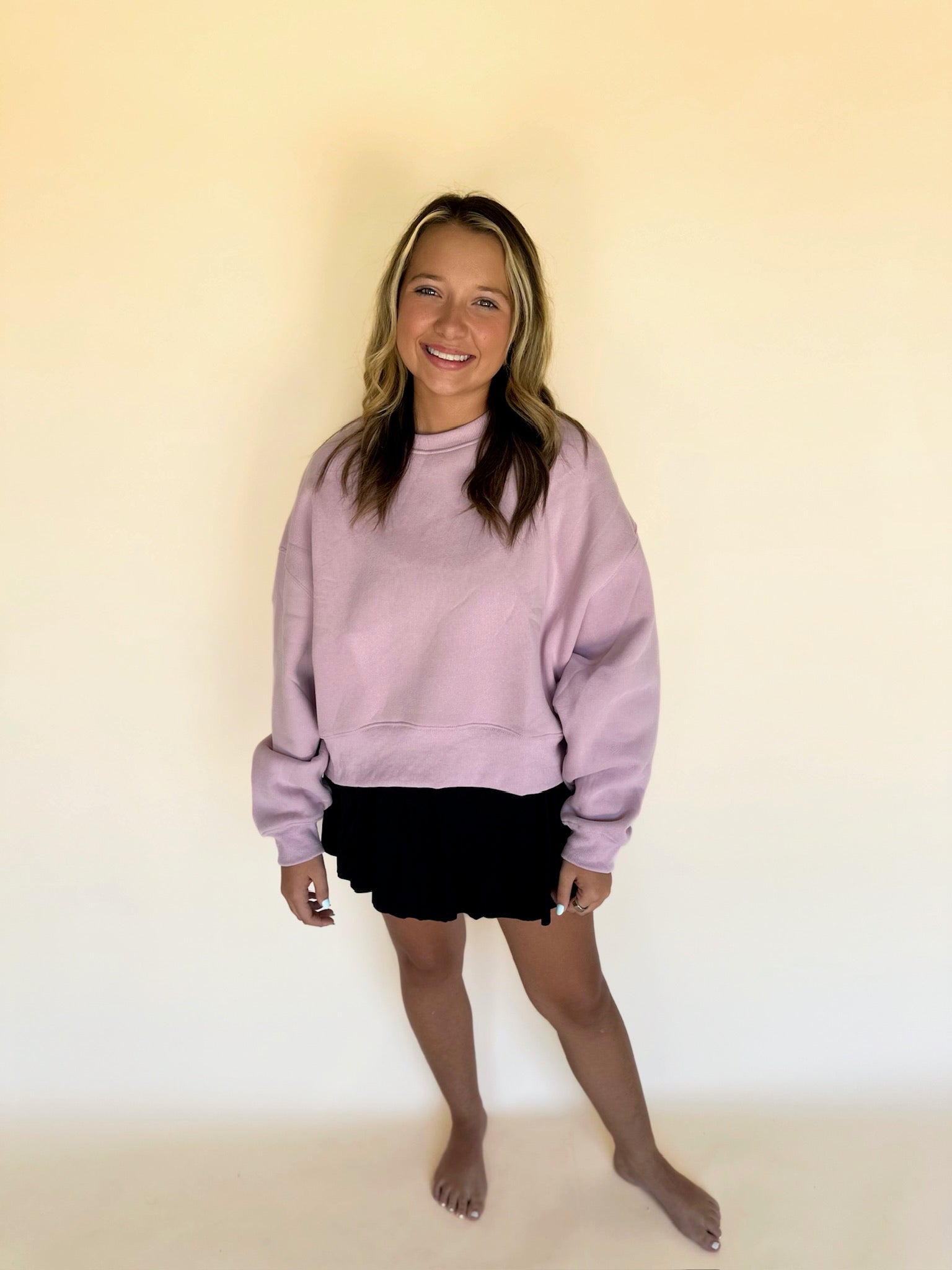 Person wearing a light purple sweatshirt and black shorts against a plain background