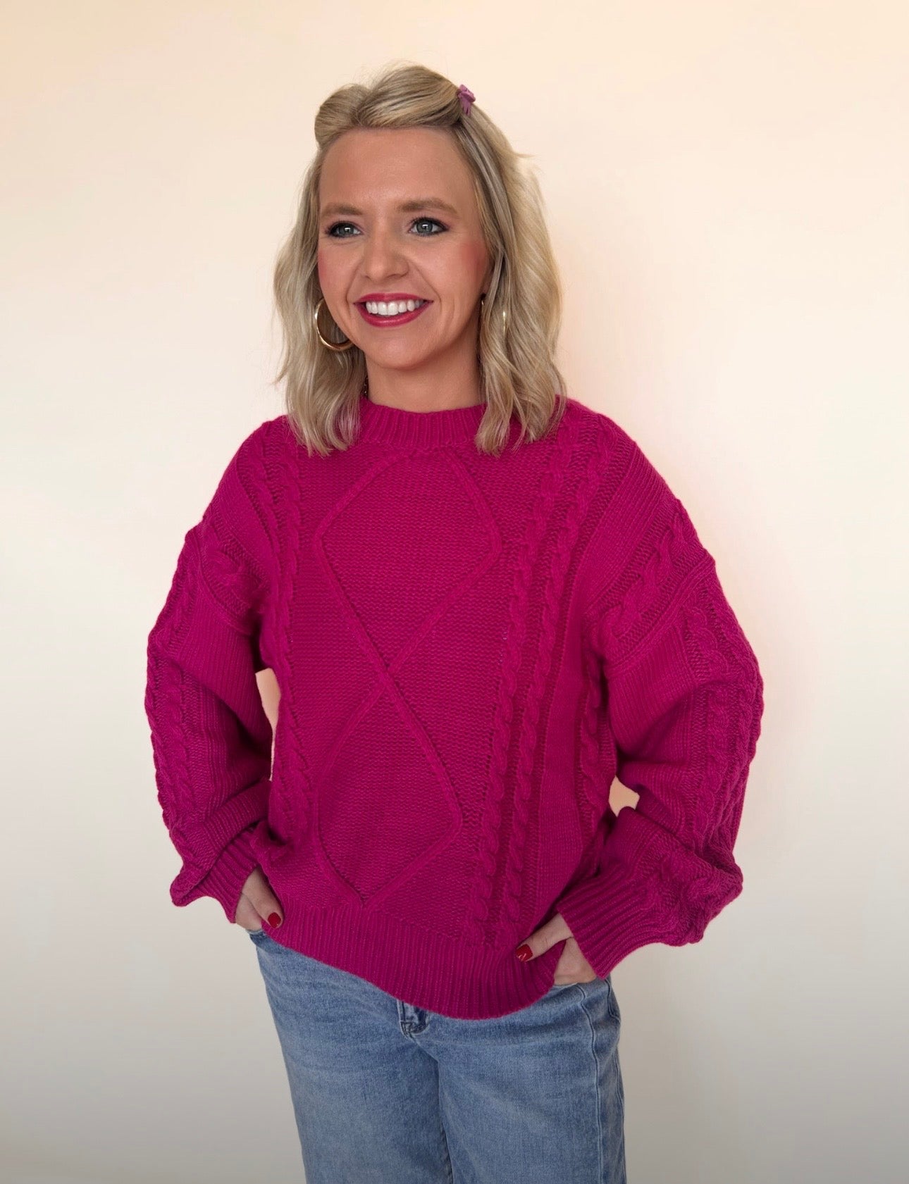 Woman wearing a pink sweater and blue jeans against a plain background