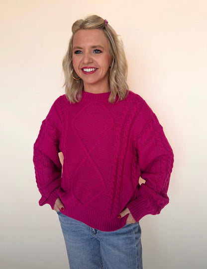 Woman wearing a pink sweater and blue jeans against a plain background