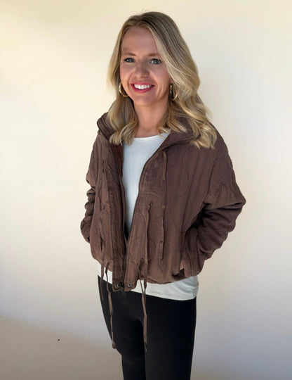 Woman wearing a brown jacket over a white shirt with a plain background