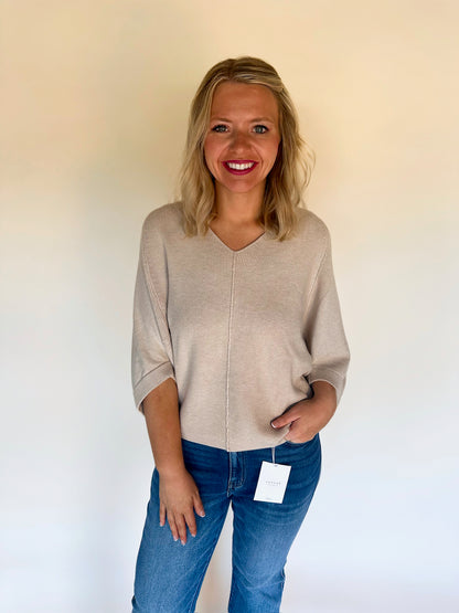 Woman wearing an oatmeal sweater and blue jeans holding a white card against a plain background