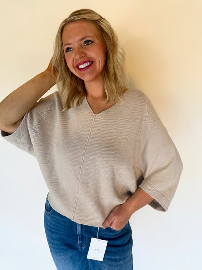 Woman wearing an oatmeal sweater and blue jeans with a plain background