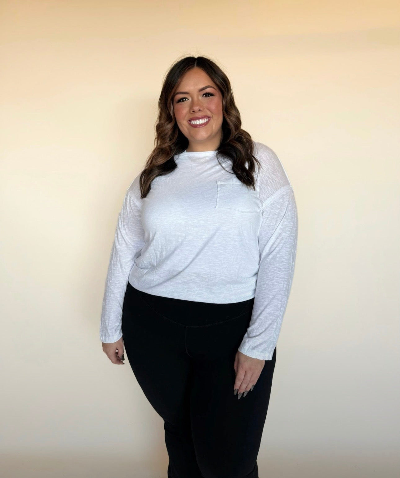 Woman wearing a white long-sleeve top and black pants against a beige background