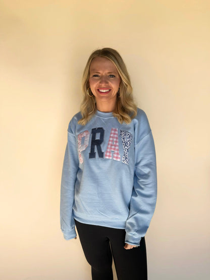 Woman wearing a light blue sweatshirt with appliqué letters spelling “PRAY,” paired with black leggings.