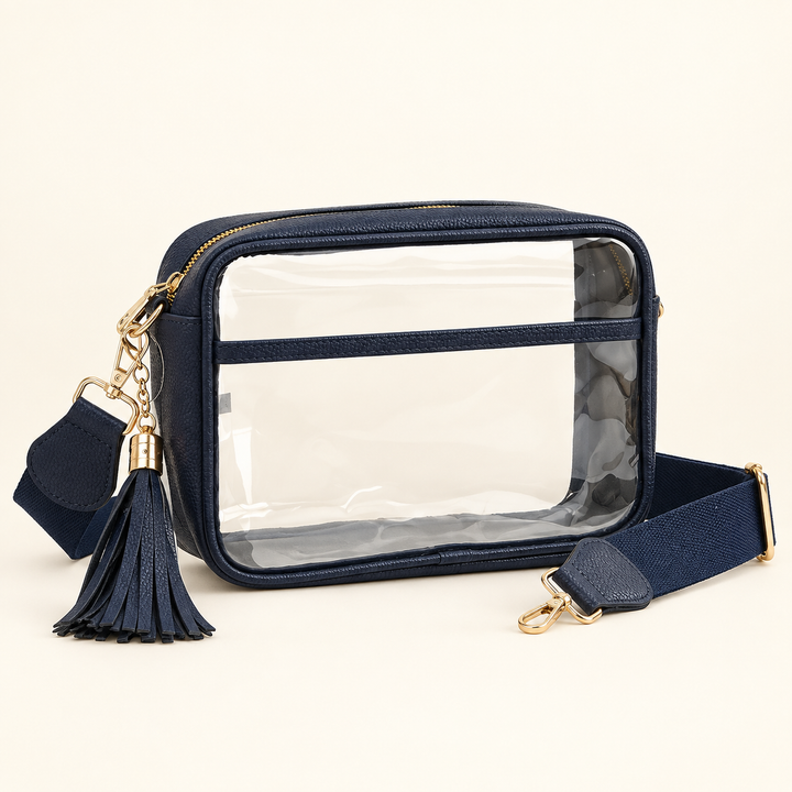 Clear stadium crossbody bag with navy trim, matching tassel and woven strap, and gold-tone hardware on a warm cream background.