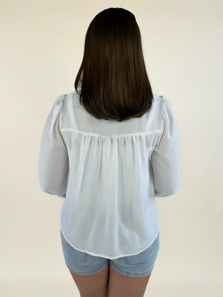 Back view of a white lightweight woven blouse with a ruffle neckline and relaxed fit.