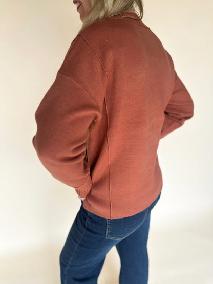 Person wearing a copper-colored jacket and blue jeans on a plain background