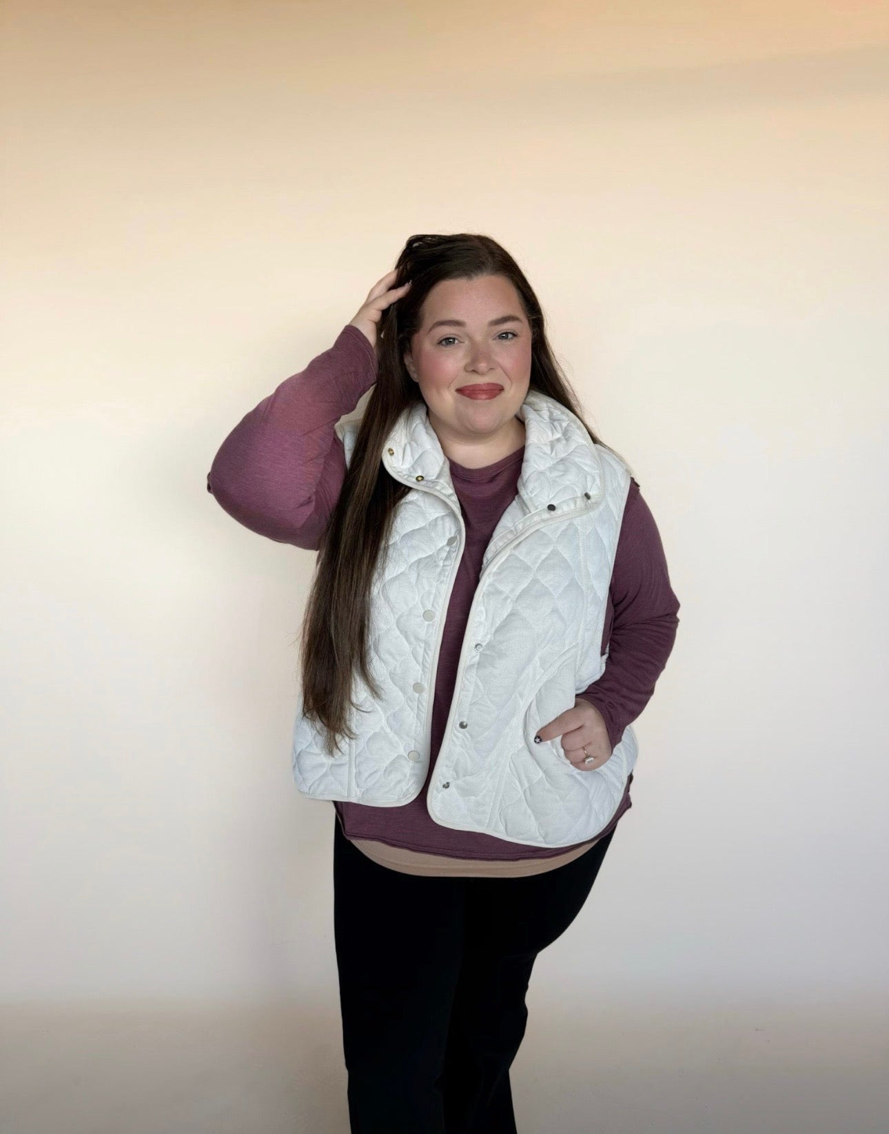 Person wearing a white quilted vest over a purple long-sleeve shirt on a plain background