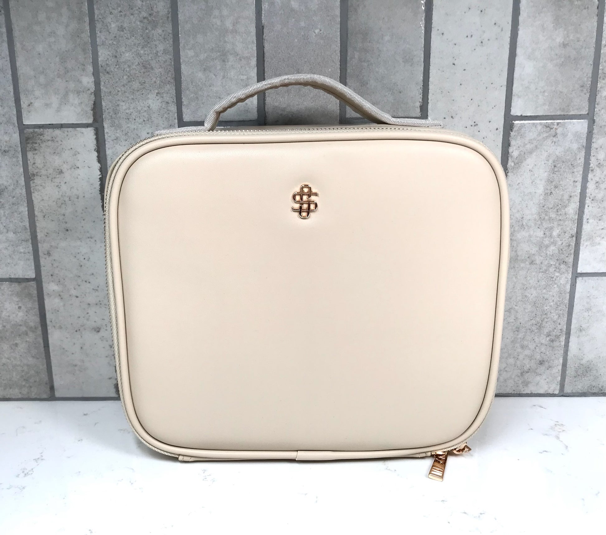 Beige cosmetic case with a brand logo on a gray tiled background