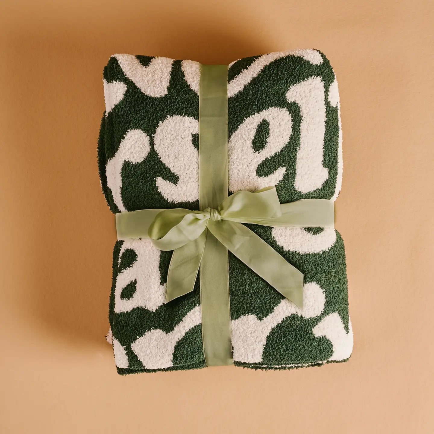 Folded green towel with white pattern and green ribbon on a beige background