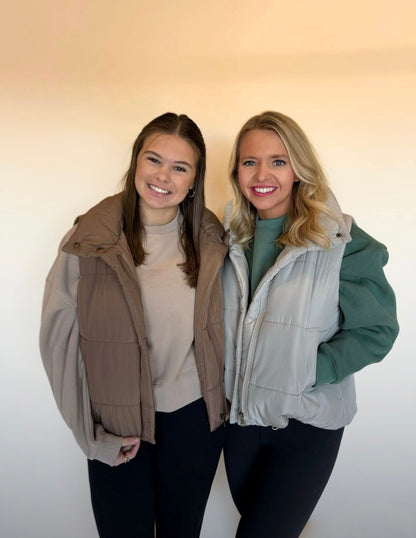 Two women wearing puffer vests against a plain background