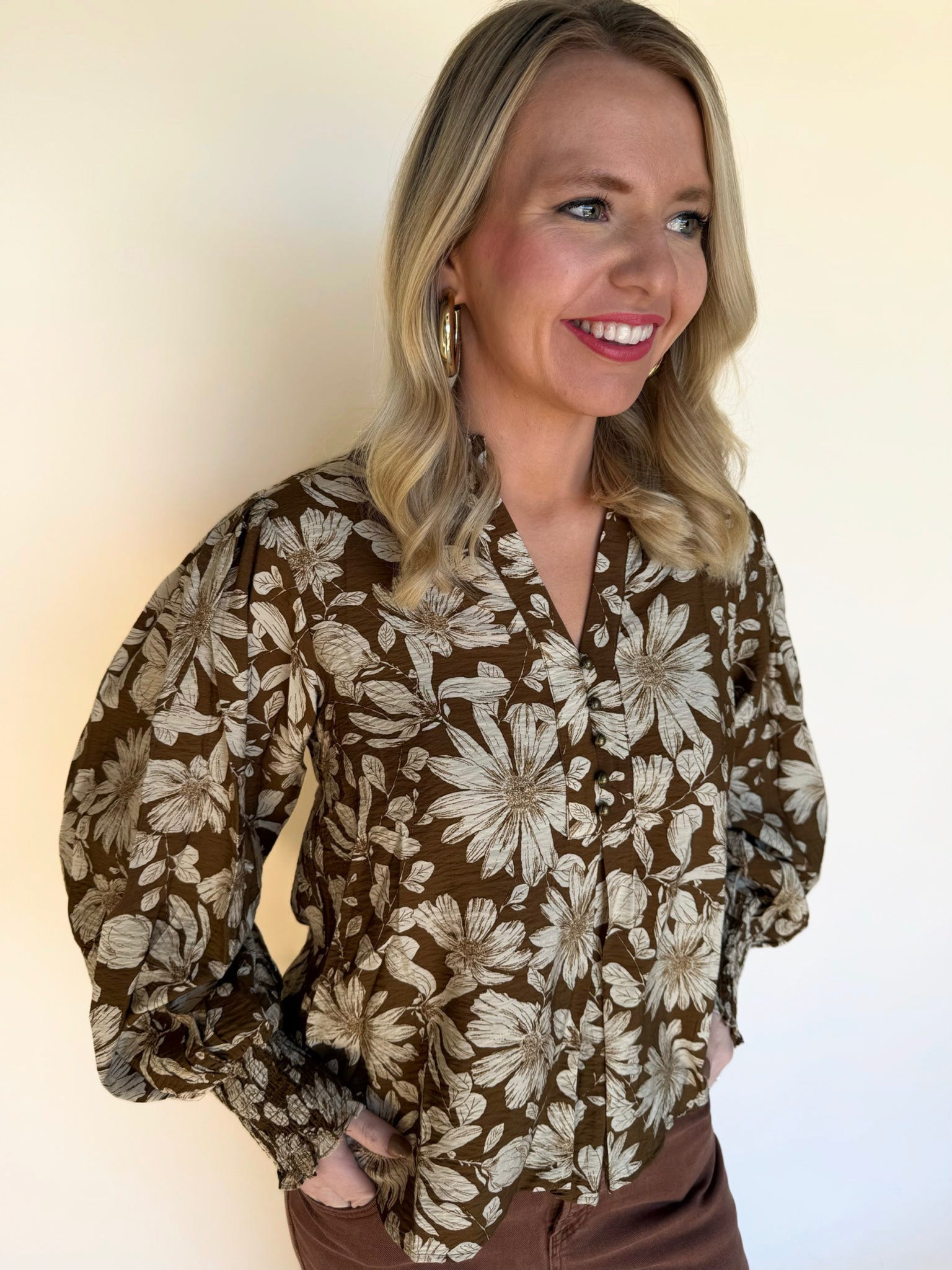 Side view close-up of a woman wearing a brown floral blouse with long puff sleeves and button-front detail.
