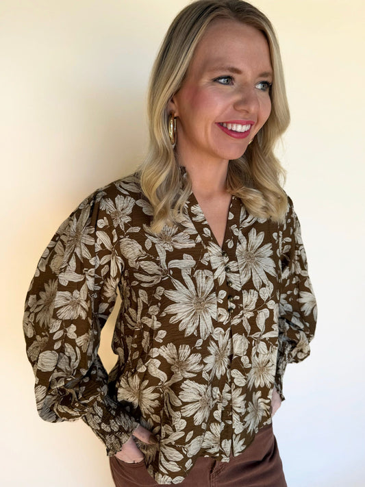 Side view close-up of a woman wearing a brown floral blouse with long puff sleeves and button-front detail.
