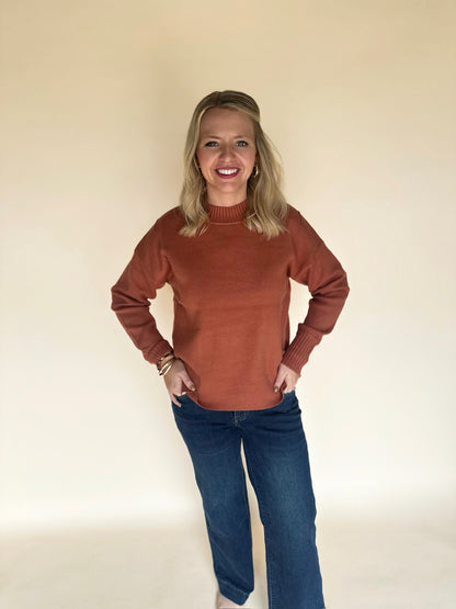 Woman wearing a copper sweater and blue jeans against a plain background