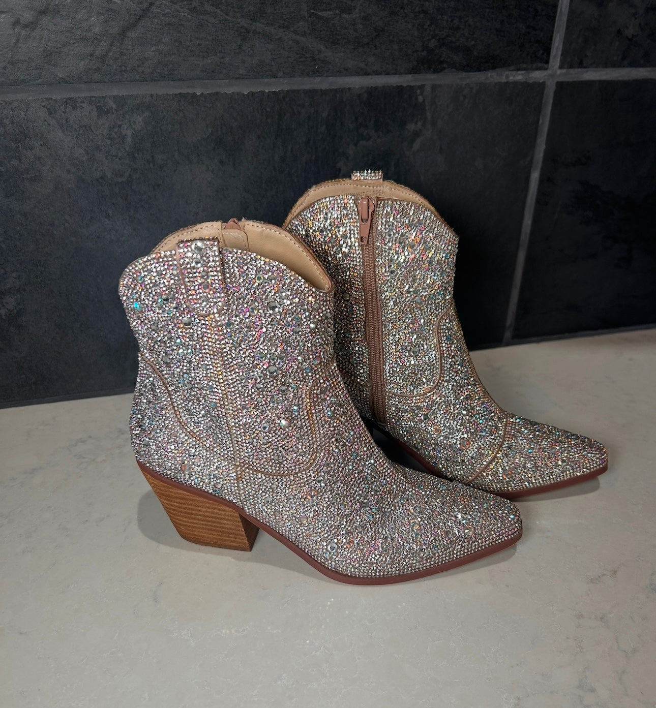 Pair of sparkling silver cowboy boots on a tiled floor.