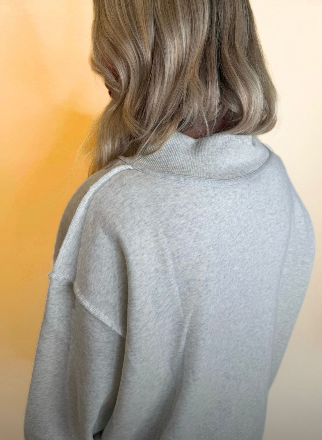 Close-up of light gray oversized sweatshirt showing drop shoulder seams and relaxed collar, soft fleece-style texture.