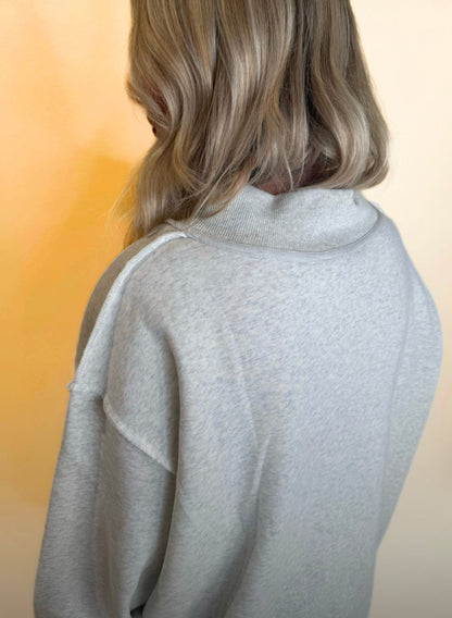 Close-up of light gray oversized sweatshirt showing drop shoulder seams and relaxed collar, soft fleece-style texture.