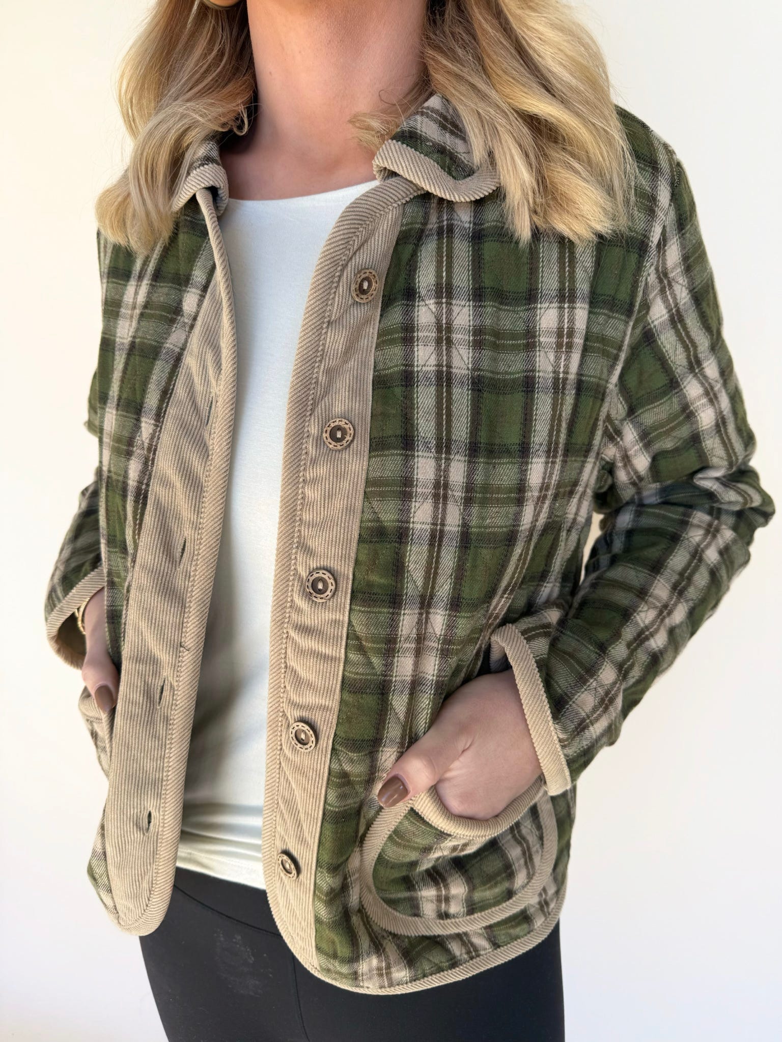 Close-up of green and tan plaid jacket featuring corduroy trim, button-down front, and curved pockets layered over a white top.