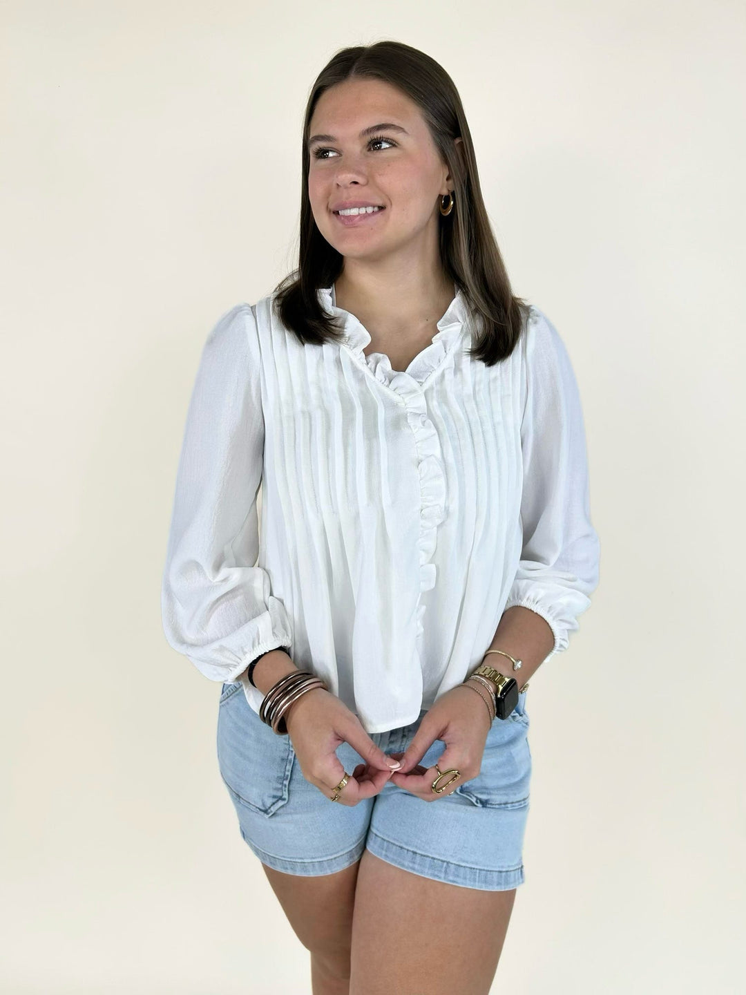 Woman wearing a white V-neck pintuck blouse with 3/4 sleeves paired with denim shorts.