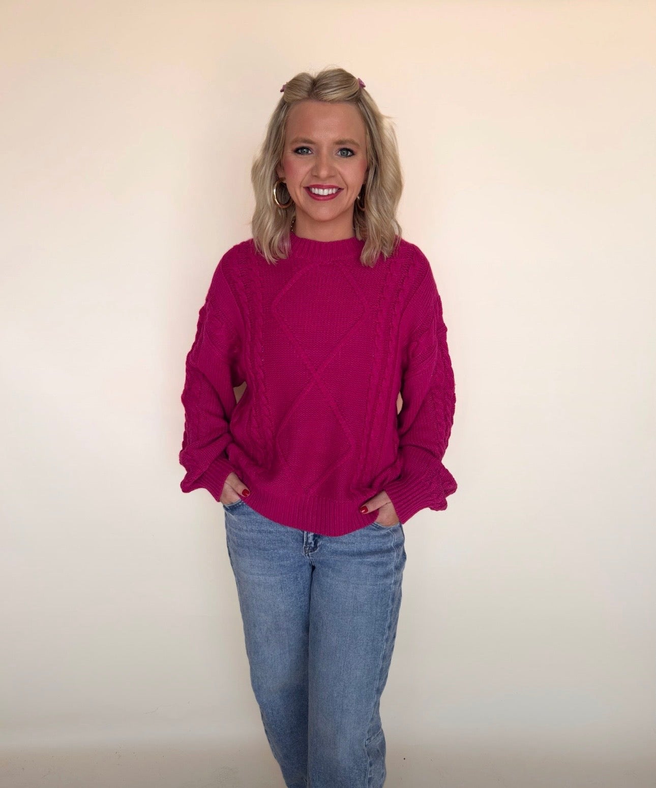 Woman wearing a magenta sweater and blue jeans against a plain background