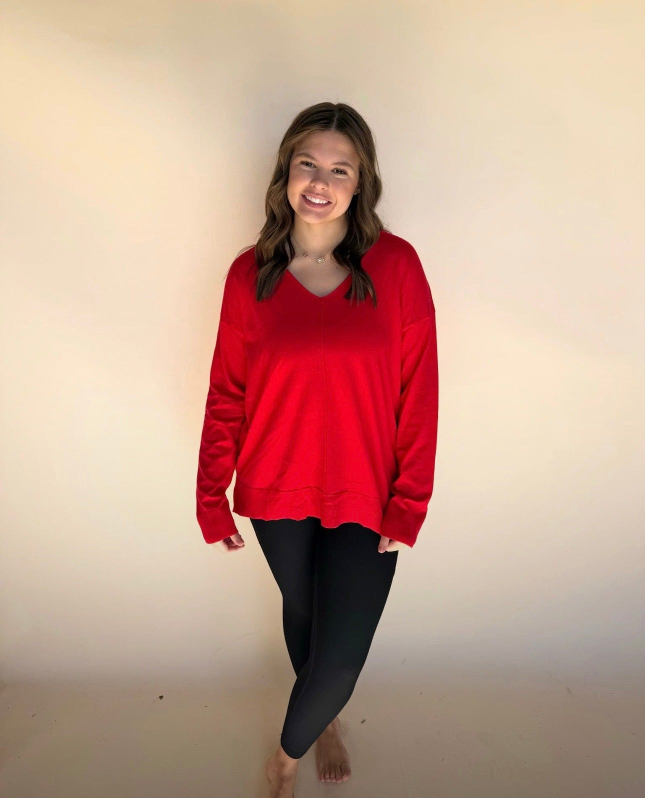 Person wearing a red sweater and black leggings against a plain background