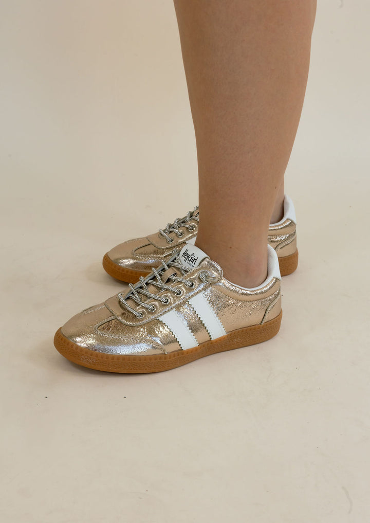 Metallic gold sneakers with white side stripes and gum soles, shown on a person&