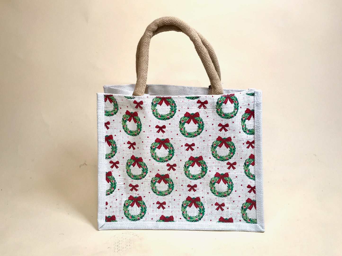White holiday tote bag with green wreath and red bow pattern, standing upright against neutral background