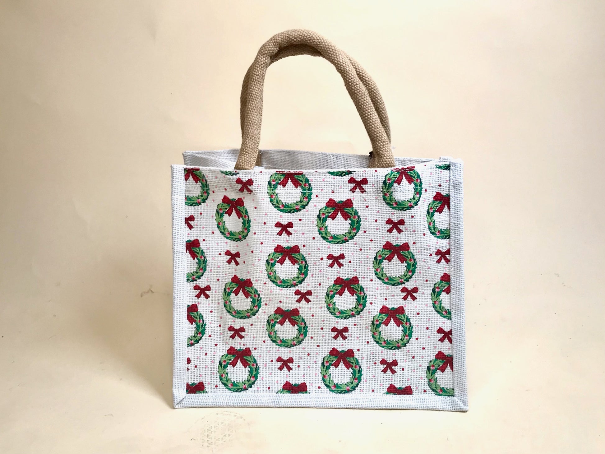 White holiday tote bag with green wreath and red bow pattern, standing upright against neutral background