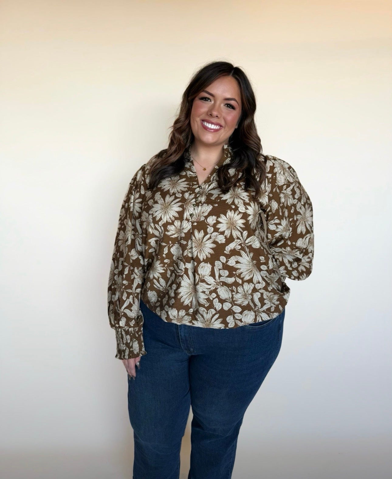 Full-body view of woman in a brown floral long-sleeve blouse with ivory flowers, styled with dark blue jeans. 
