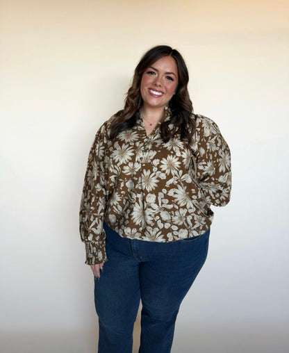 Full-body view of woman in a brown floral long-sleeve blouse with ivory flowers, styled with dark blue jeans. 