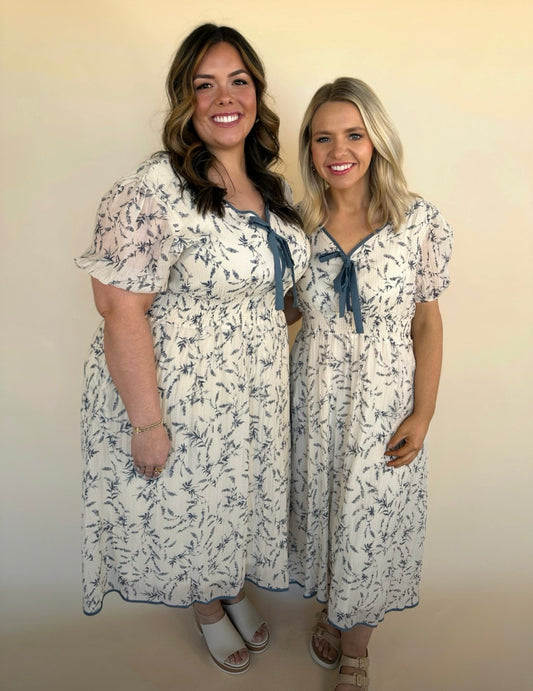 Zoya Floral Bow Dress in soft blue floral print with smocked waist and front tie bow detail – two models front view