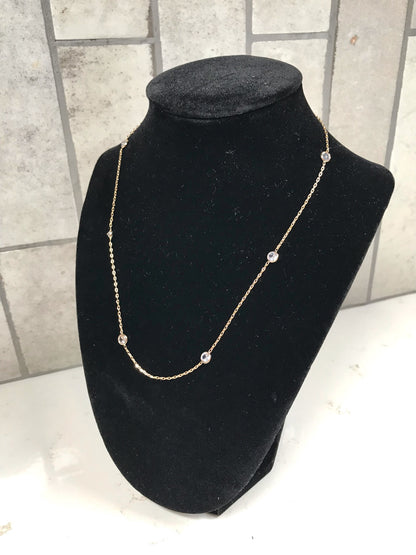 Gold dainty station necklace with small bezel-set clear crystals displayed on a black velvet necklace stand against a light tile background.