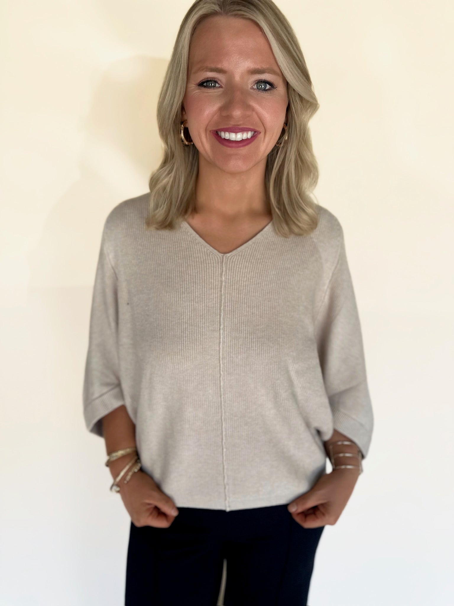 Woman wearing an oatmeal  sweater against a plain background