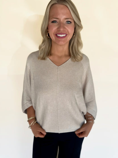 Woman wearing an oatmeal  sweater against a plain background