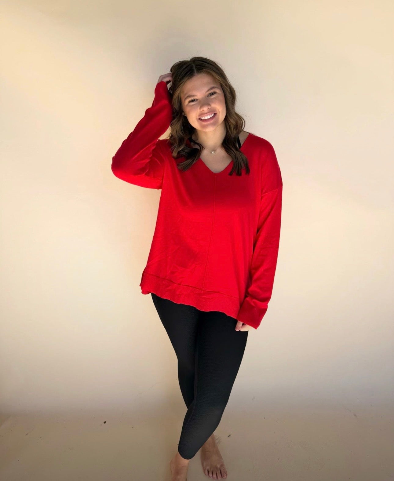 Person wearing a red sweatshirt and black leggings against a plain background