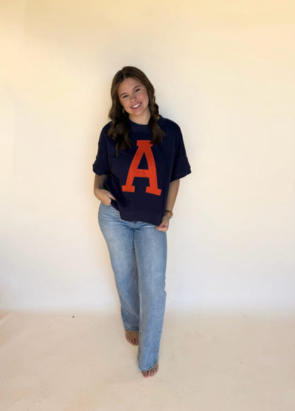 Person wearing a navy blue t-shirt with a large orange 'A' and blue jeans against a plain background