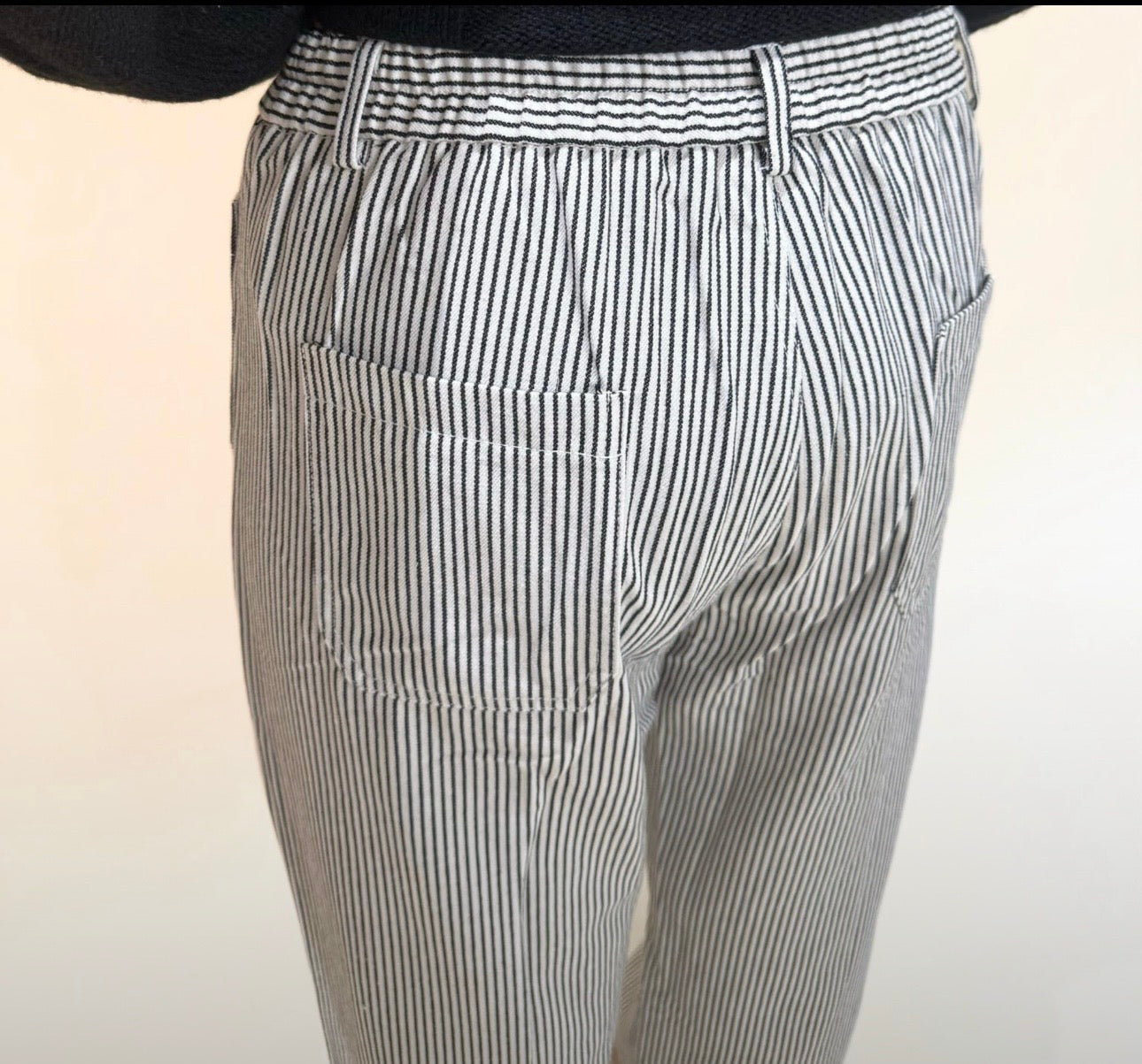 Close-up back view of black and white vertical stripe pants highlighting waistband, belt loops, and back pocket stitching.