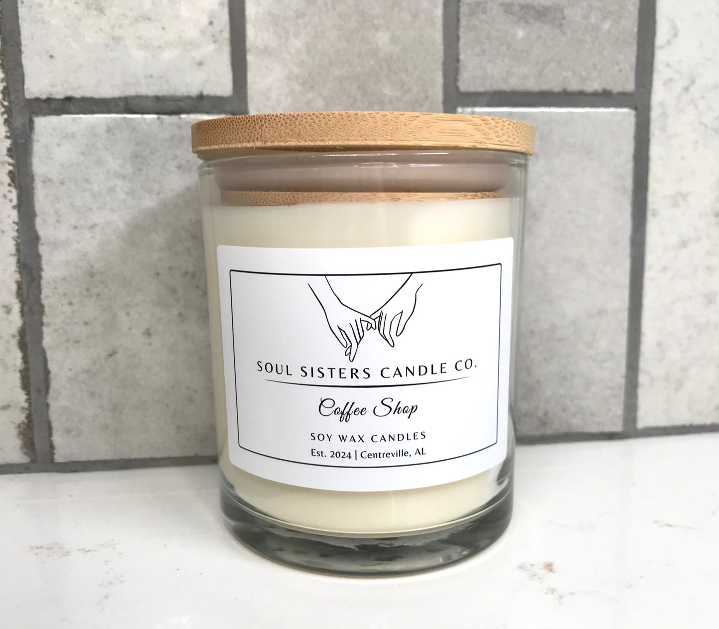 Scented candle with a wooden lid and 'Soul Sisters Candle Co.' label on a tiled wall background