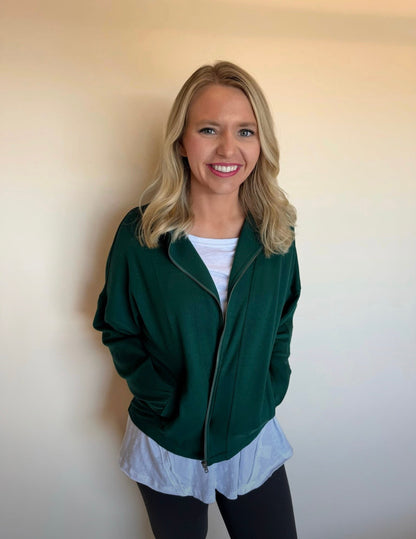 Woman wearing a green jacket over a white shirt against a plain background
