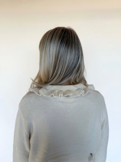 Back view of a cream knit cardigan featuring a ruffled collar detail, shown against a plain neutral background.