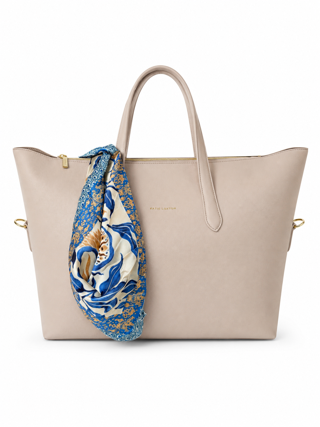 A light beige leather tote bag with double top handles and gold-tone hardware, featuring a blue and white patterned silk scarf tied to one handle, set against a plain white background.