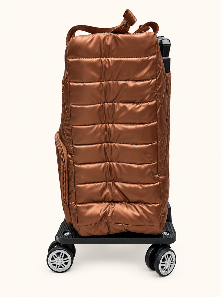 Side view of Simply Southern copper swivel rolling tote showing metallic bronze fabric, horizontal padded quilting, side zipper pocket, and spinner wheels.