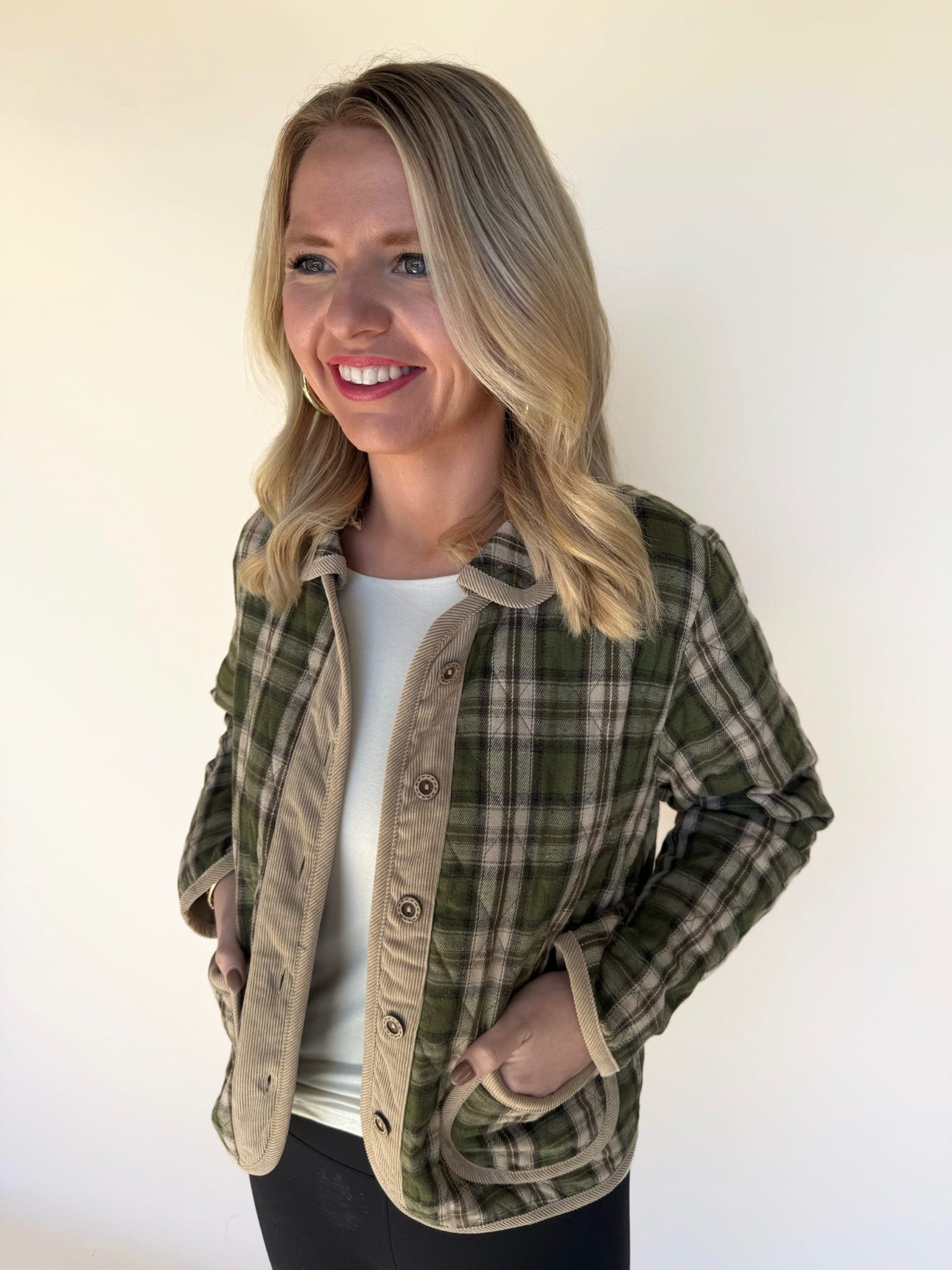 Woman wearing a green and tan plaid button-front jacket with corduroy trim, standing angled with hands in pockets — casual fall layering piece.