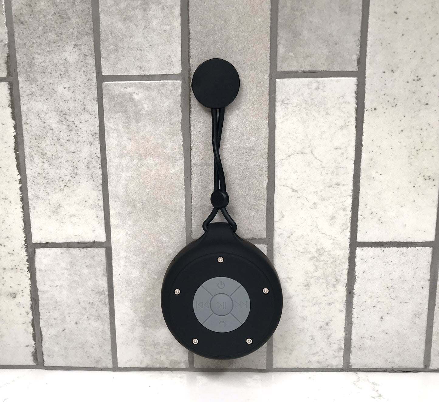 Black Bluetooth speaker with a lanyard on a tiled floor