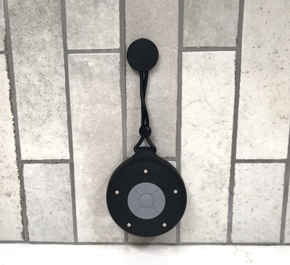 Black Bluetooth speaker with a lanyard on a tiled floor