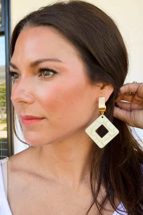 Woman wearing a gold and beige earring with a diamond-shaped center.