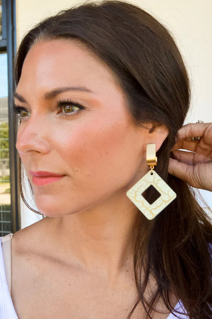 Woman wearing a gold and beige earring with a diamond-shaped center.