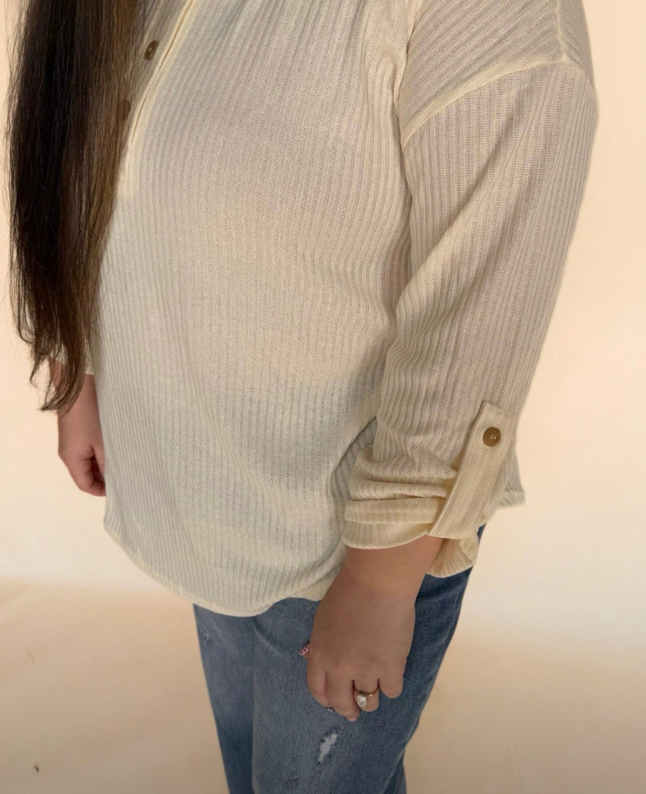 Close-up of cream ribbed Henley showing roll-tab sleeve detail and relaxed fit paired with distressed denim.