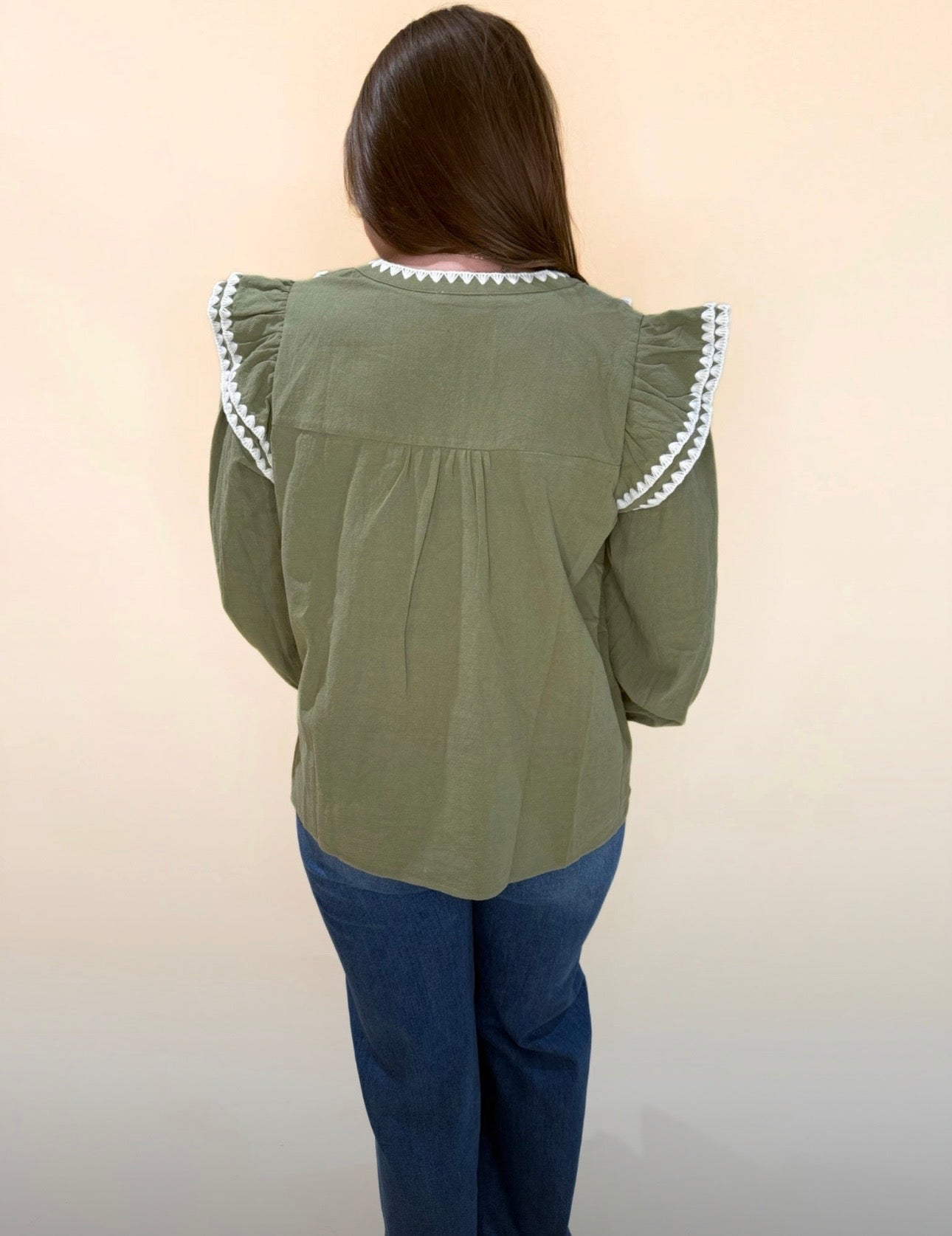 Back view of olive green blouse with ruffled shoulders and cream trim, styled casually with denim jeans.